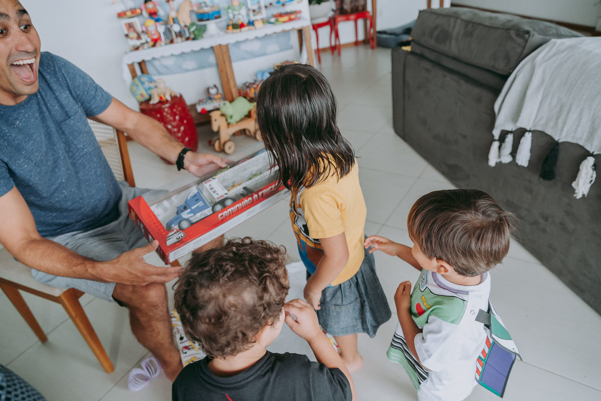 pai sorri feliz para crianças enquanto abre o presente de um dos filhos