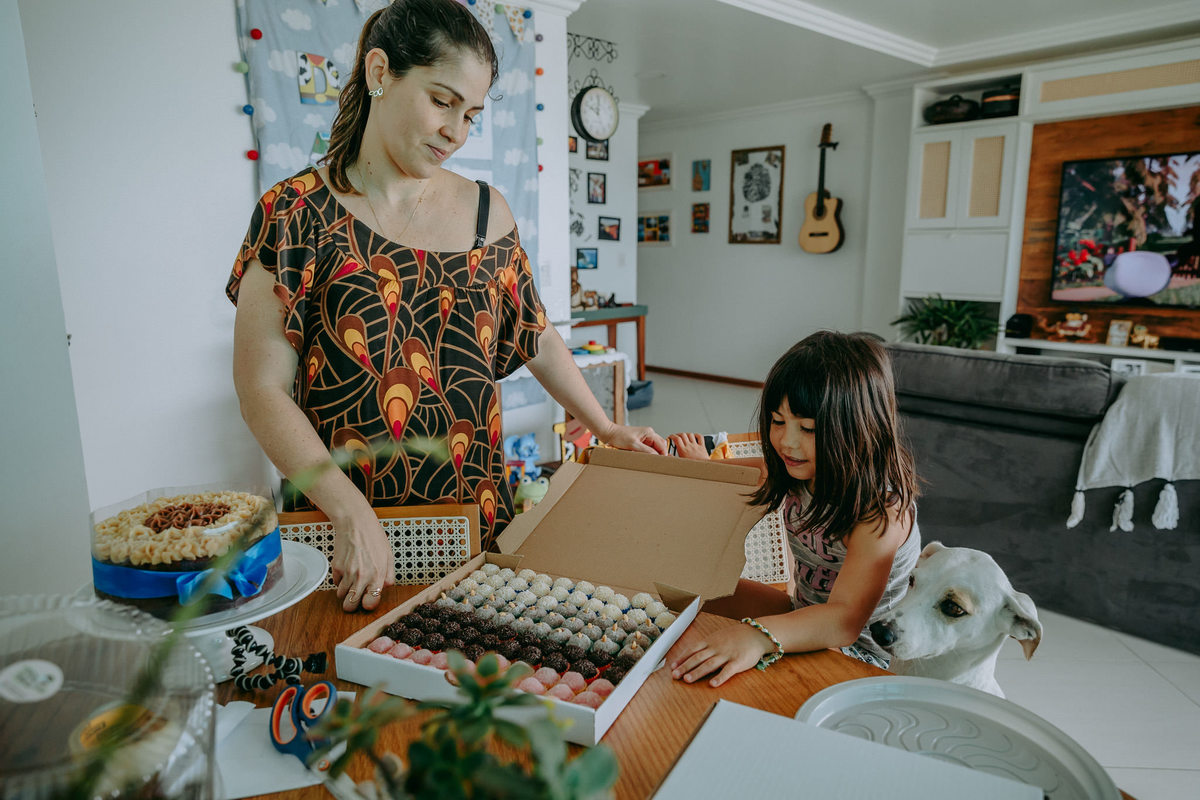 foto documental de mãe, filha e cachorro olhando os docinhos da festa 