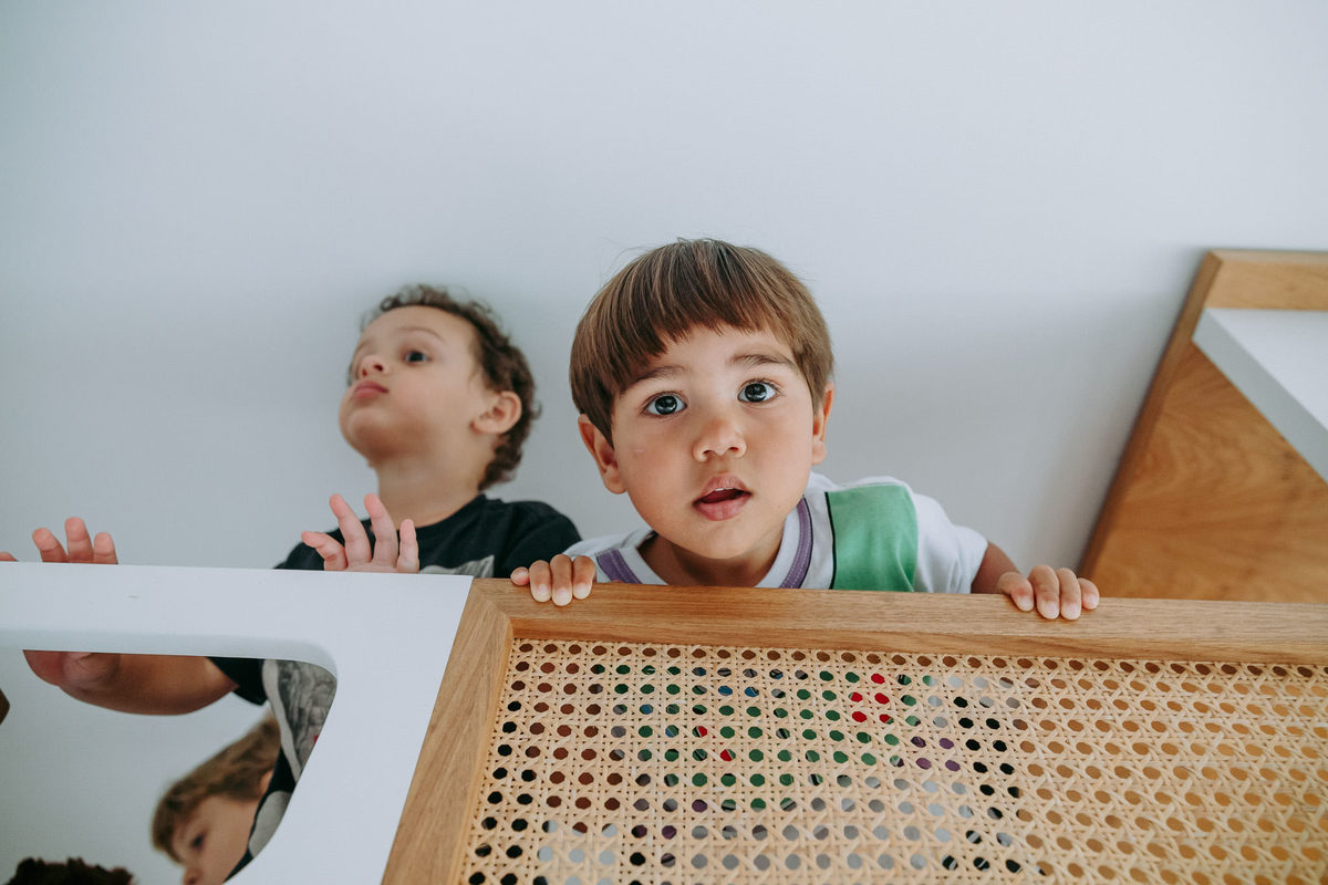 duas crianças no alto da cama em que uma delas encara a camera fotografica