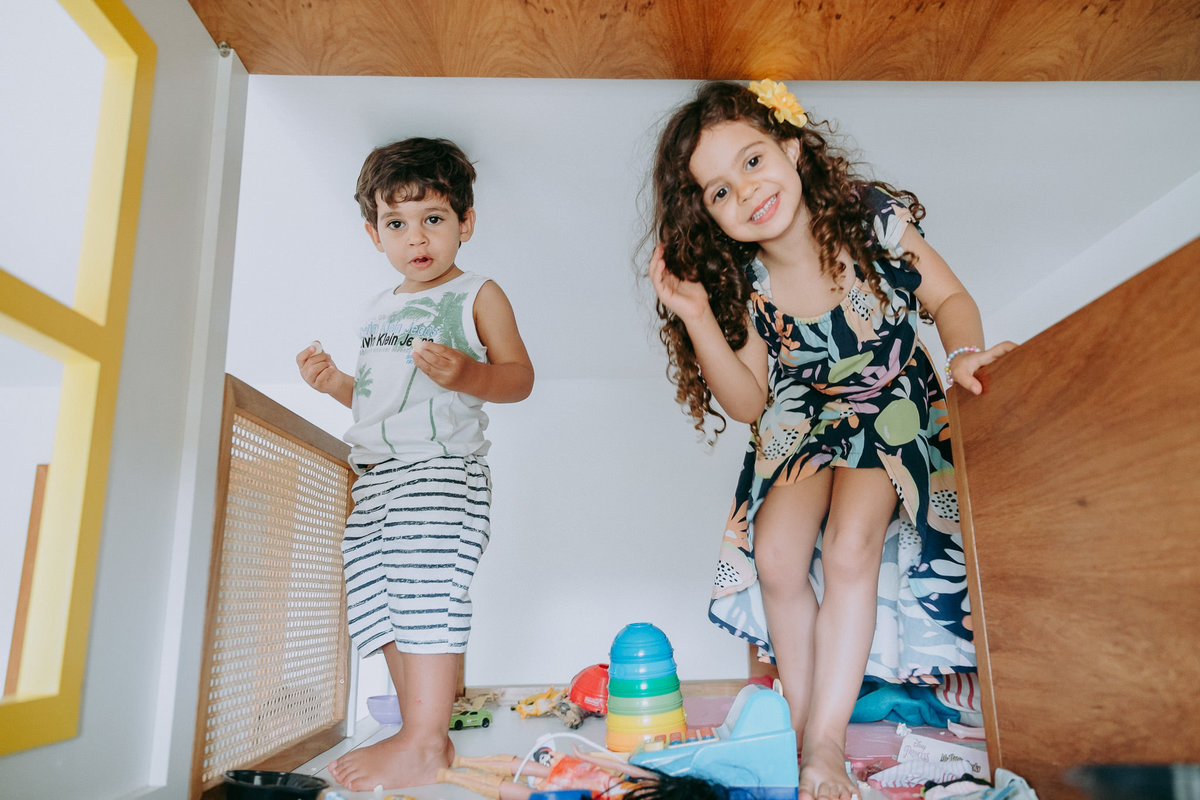 duas criancas em pe sobre uma cama casinha, uma sorrindo e a outra séria