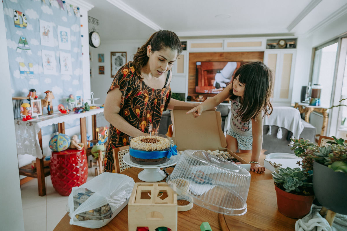 foto documental de criança mostrando pra mãe a supresa que ela colocou como enfeite de topo de bolo de aniversário