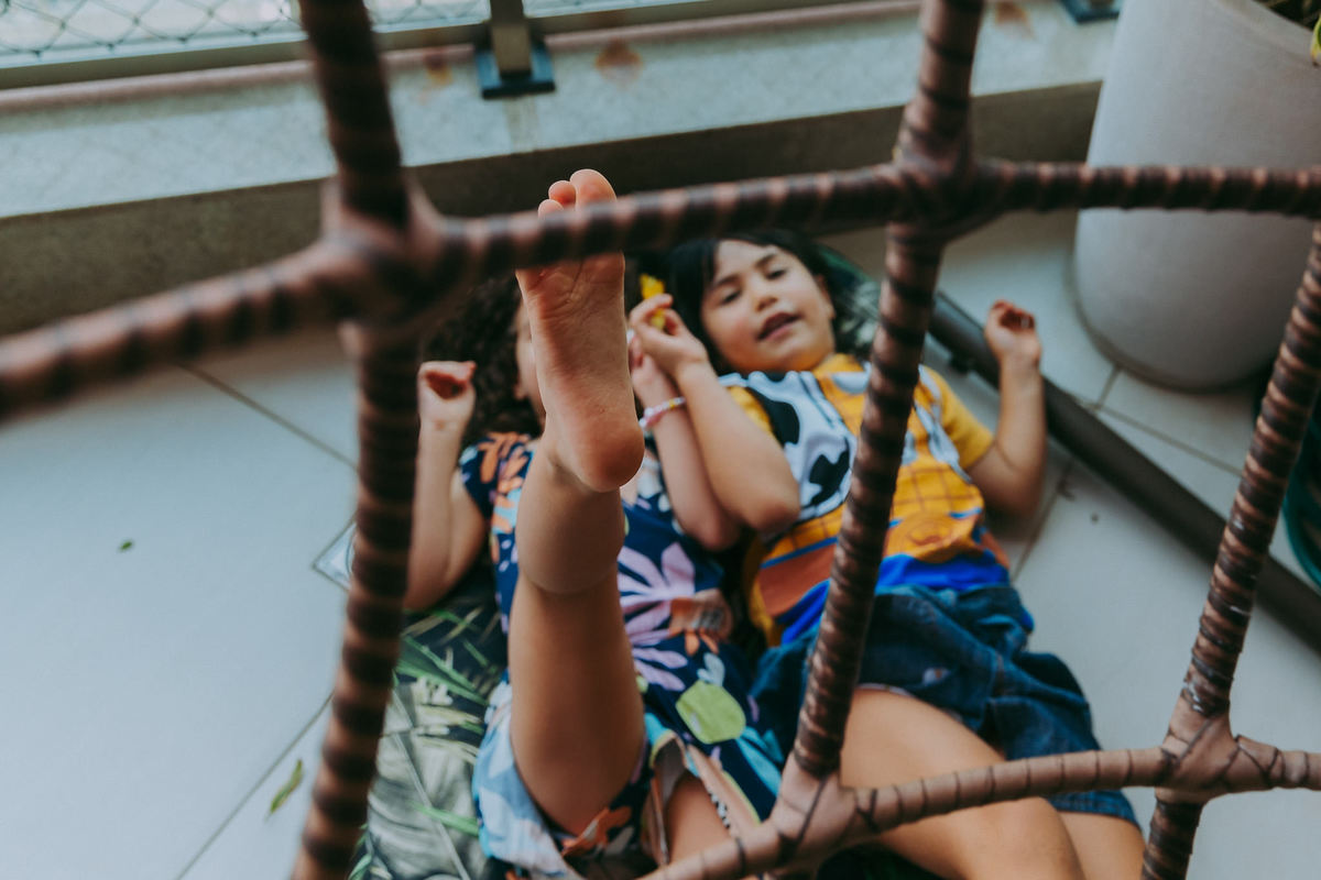 duas meninas deitadas no chao empurrando com o pé uma cadeira de balanço de teto