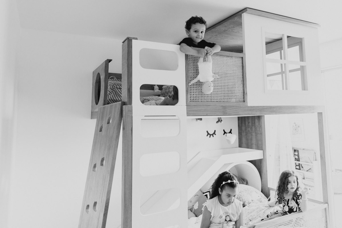 menino do alto da cama se prepara para jogar boneca na cabeça de menina sentada na parte de baixo da cama