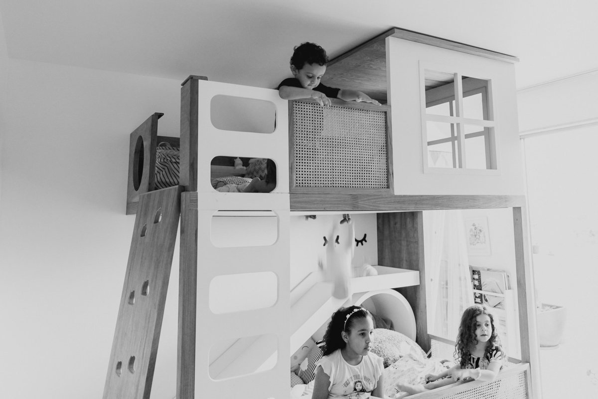 menino do alto da cama joga boneca na cabeça de menina sentada na parte de baixo da cama