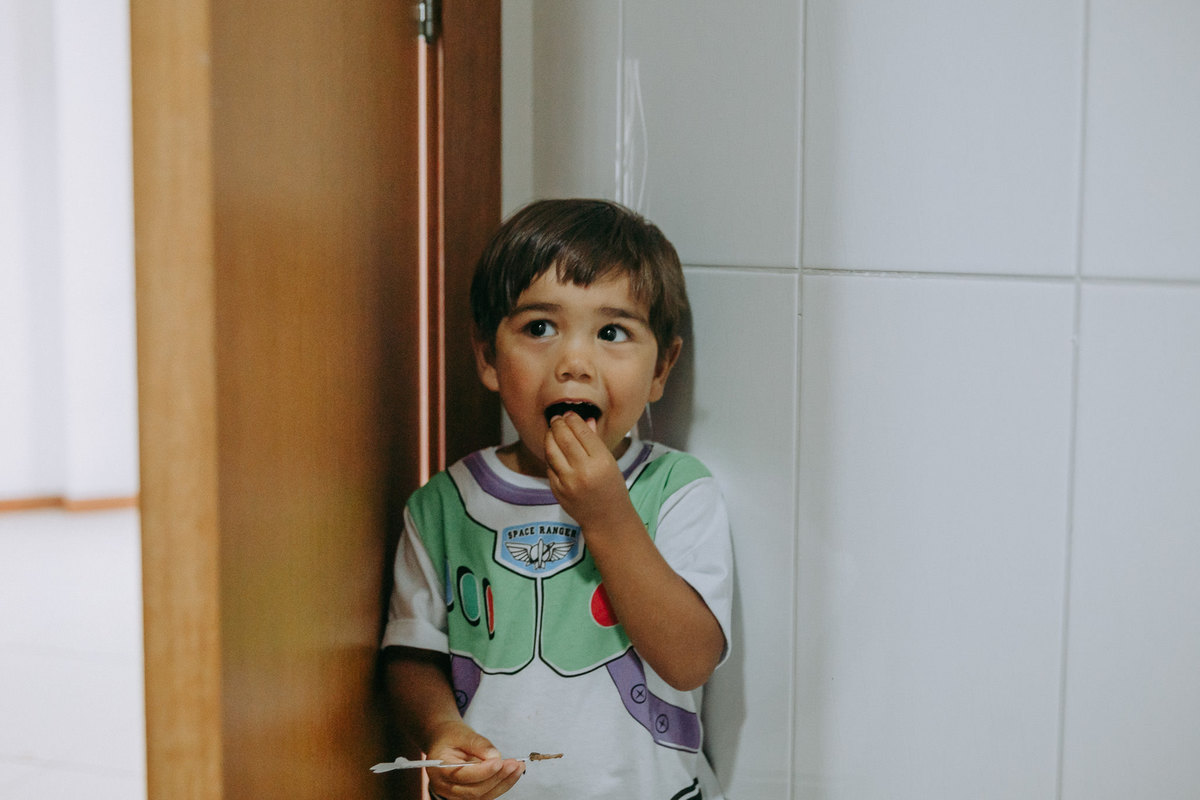 menino comendo brigadeiro escondido atras da porta 