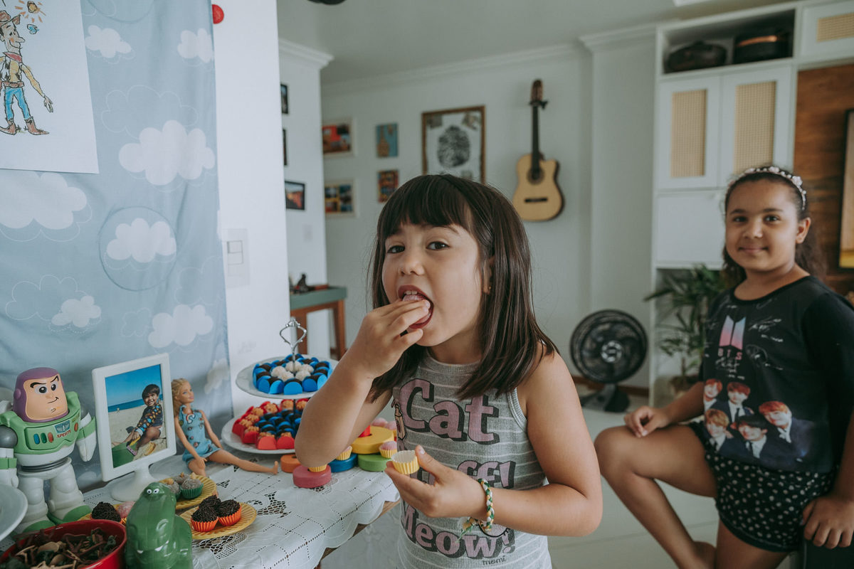 foto documental de menina devorando docinho da mesa do bolo do irmão ainda em arrumação