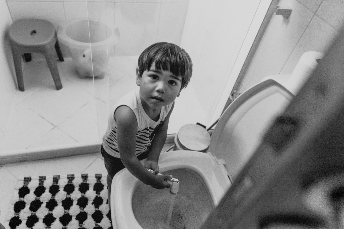 menino de 2 anos brinca com chuveirinho de vaso sanitário em banheiro de sua casa