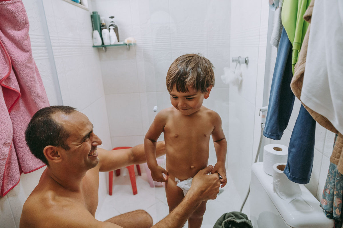 foto documental de pai tirando a fralda de filho de 2 anos para dar banho nele