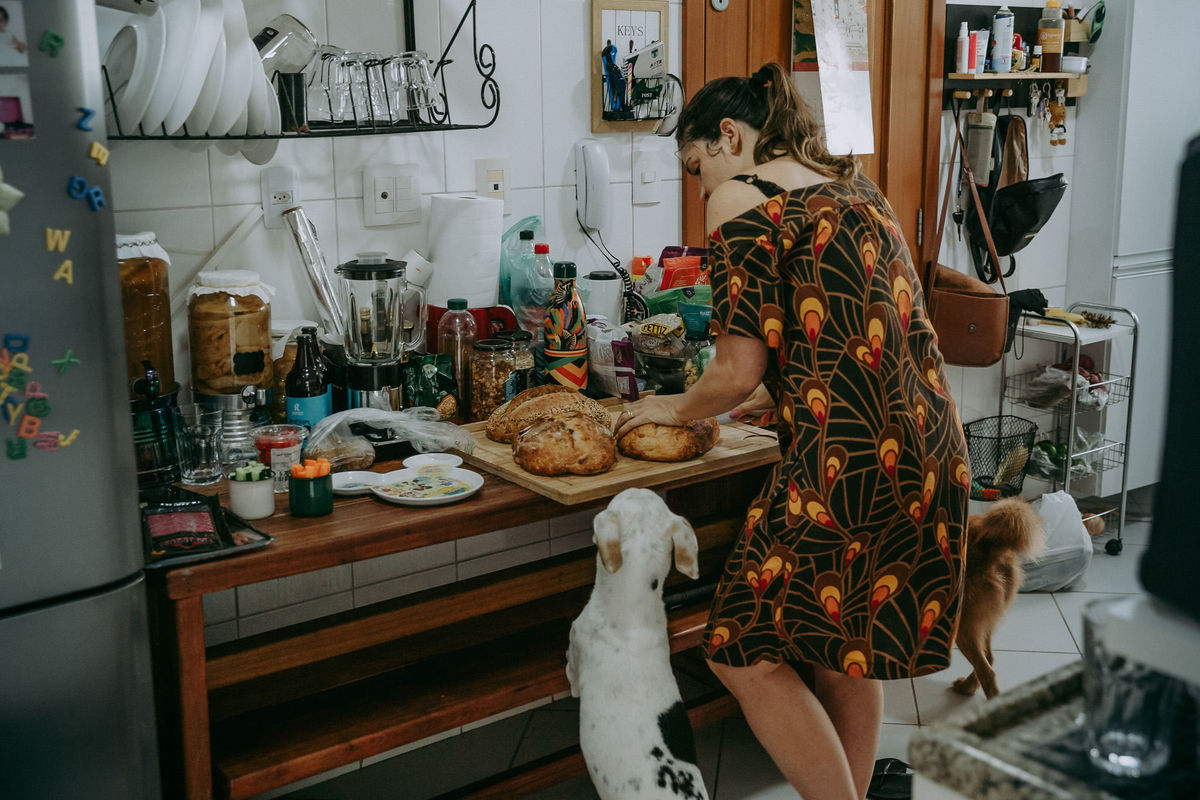foto documental de cachorro observando a dona preparar lanche com pães na cozinha de seu apartamento no recreio dos bandeirantes