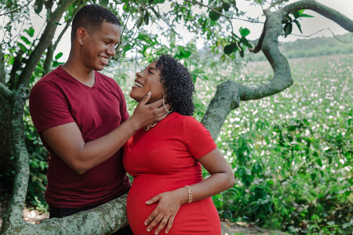 casal gestante se olha de forma romantica apoiados em arvore de tronco retorcido no parque chico mendes
