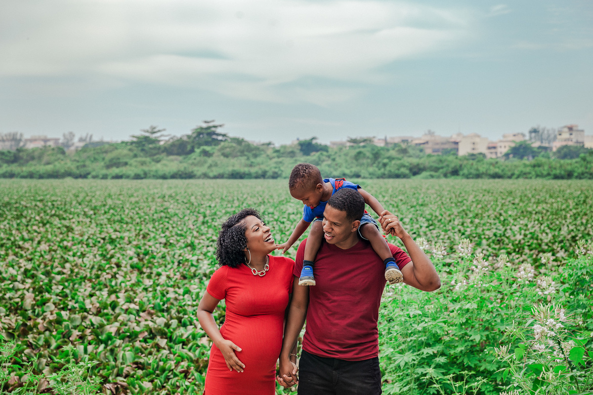familia composta de mãe gestante, pai e filho na carcunda do pai caminham em frente a lagoa de marapendi no recreio dos bandeirantes no rj