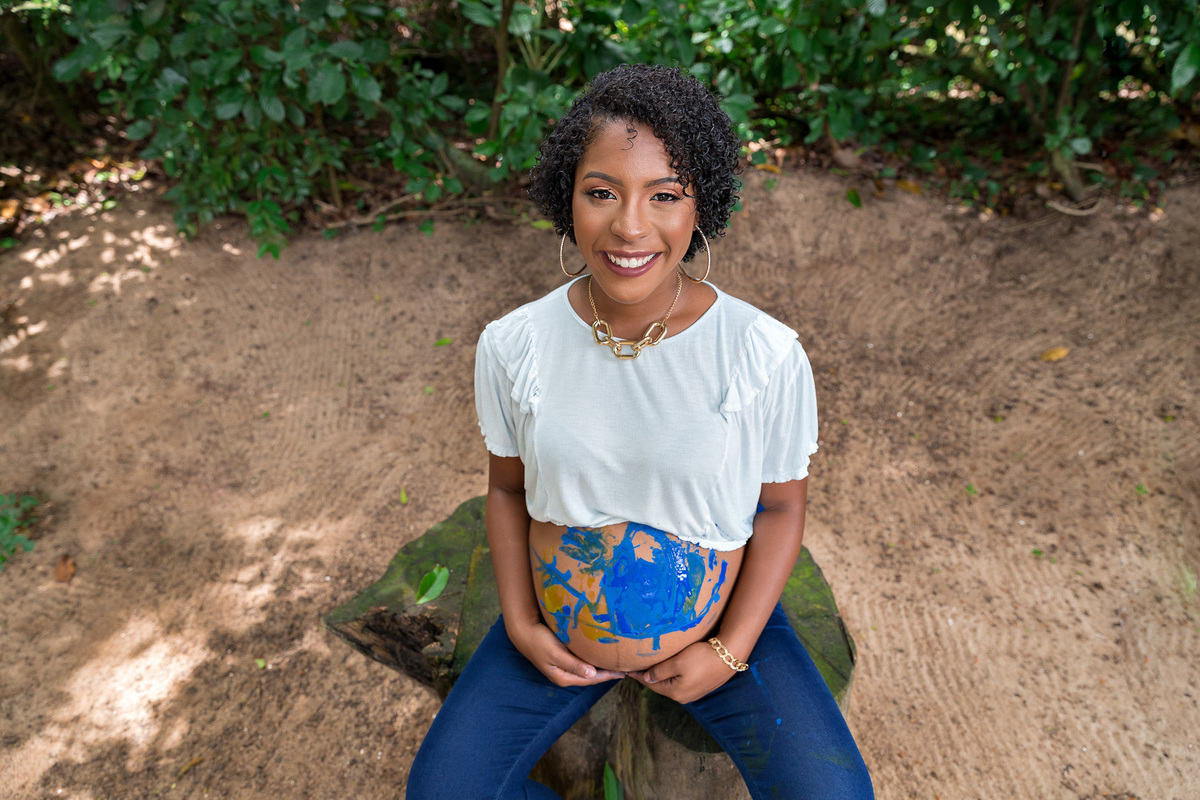 foto em plongee de gestante com a barriga pintada a mostra olhand o para a foto no fim de seu ensaio gestante no rj