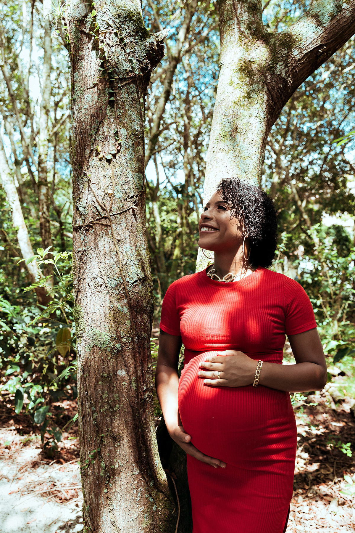 gestante de vestido vermelho olha para o alto e sorri com as maos sobre a barriga em ensaio fotografico