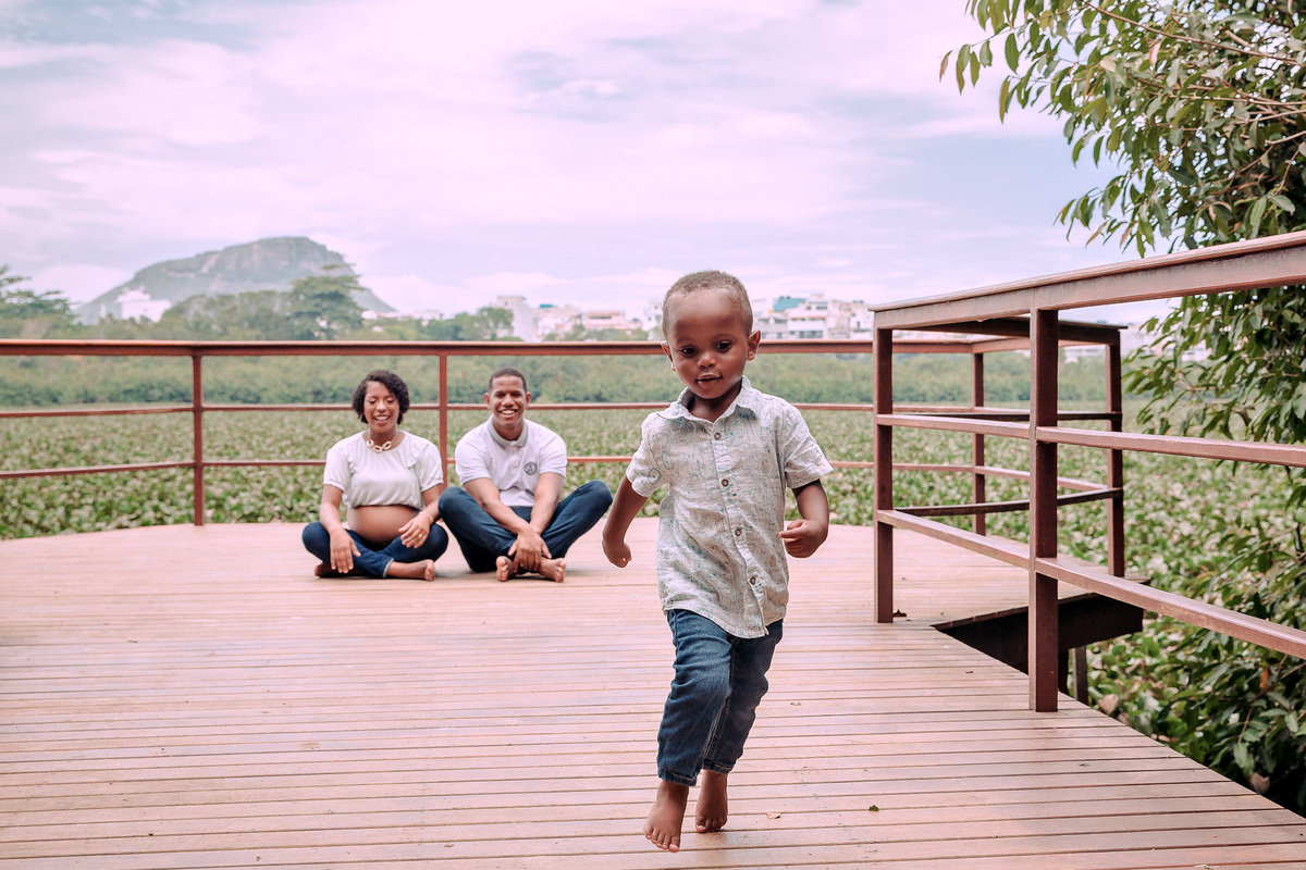 criança corre em direção à camera enquanto os pais estão sentados ao fundo olhando