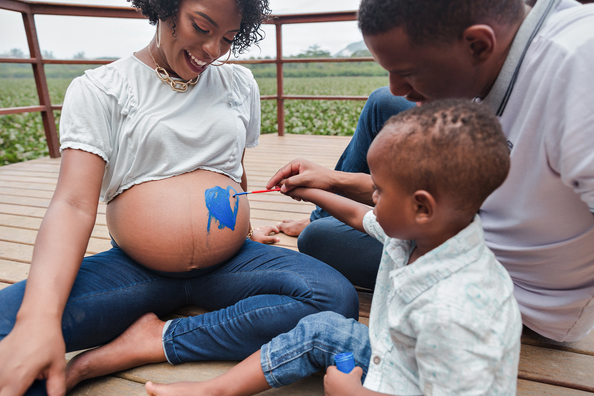 menino pinta com pincel a barriga de gravida de sua mae