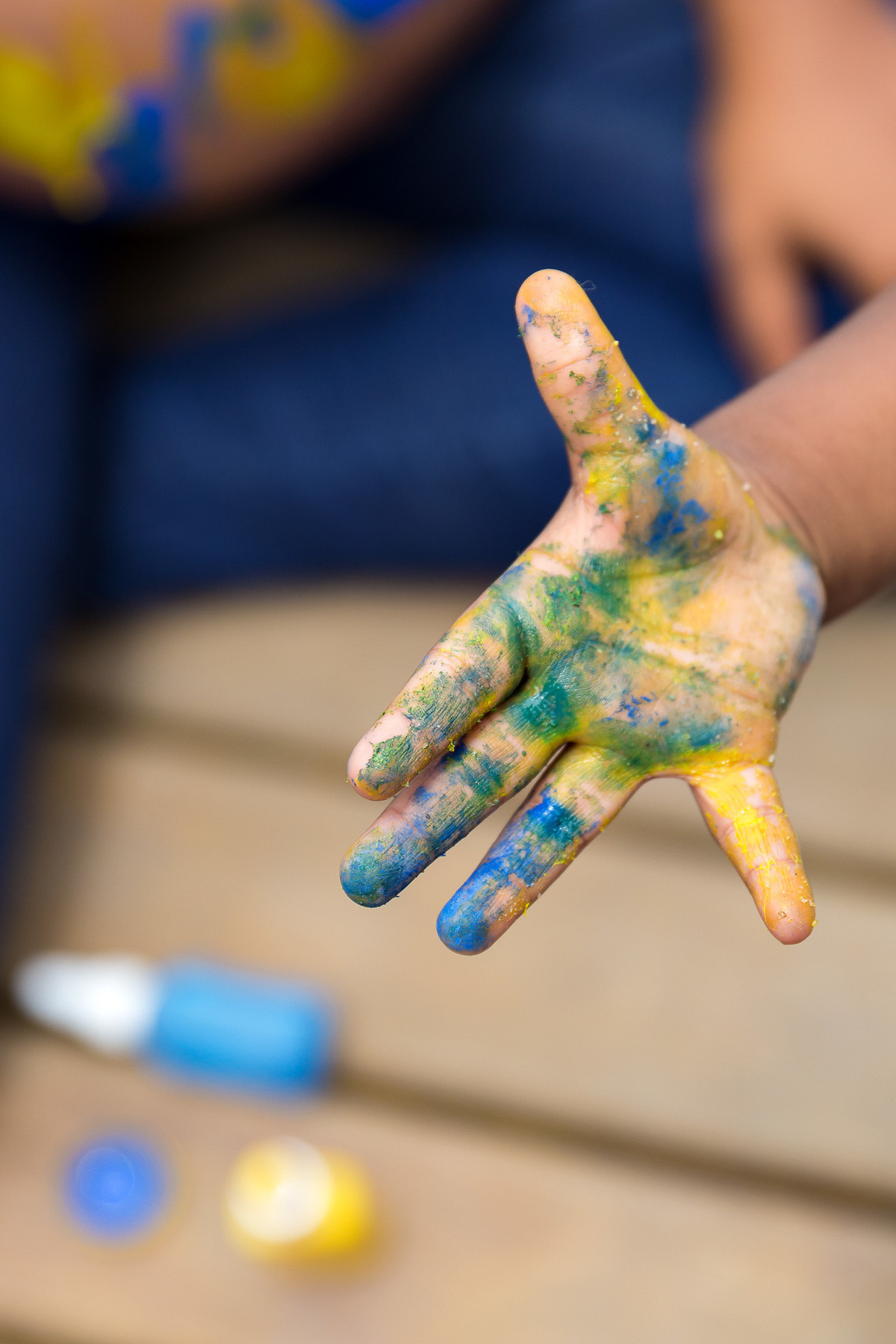 detalhe da mão de um menino de 2 anos suja de tinta nas cores azul e amarelo