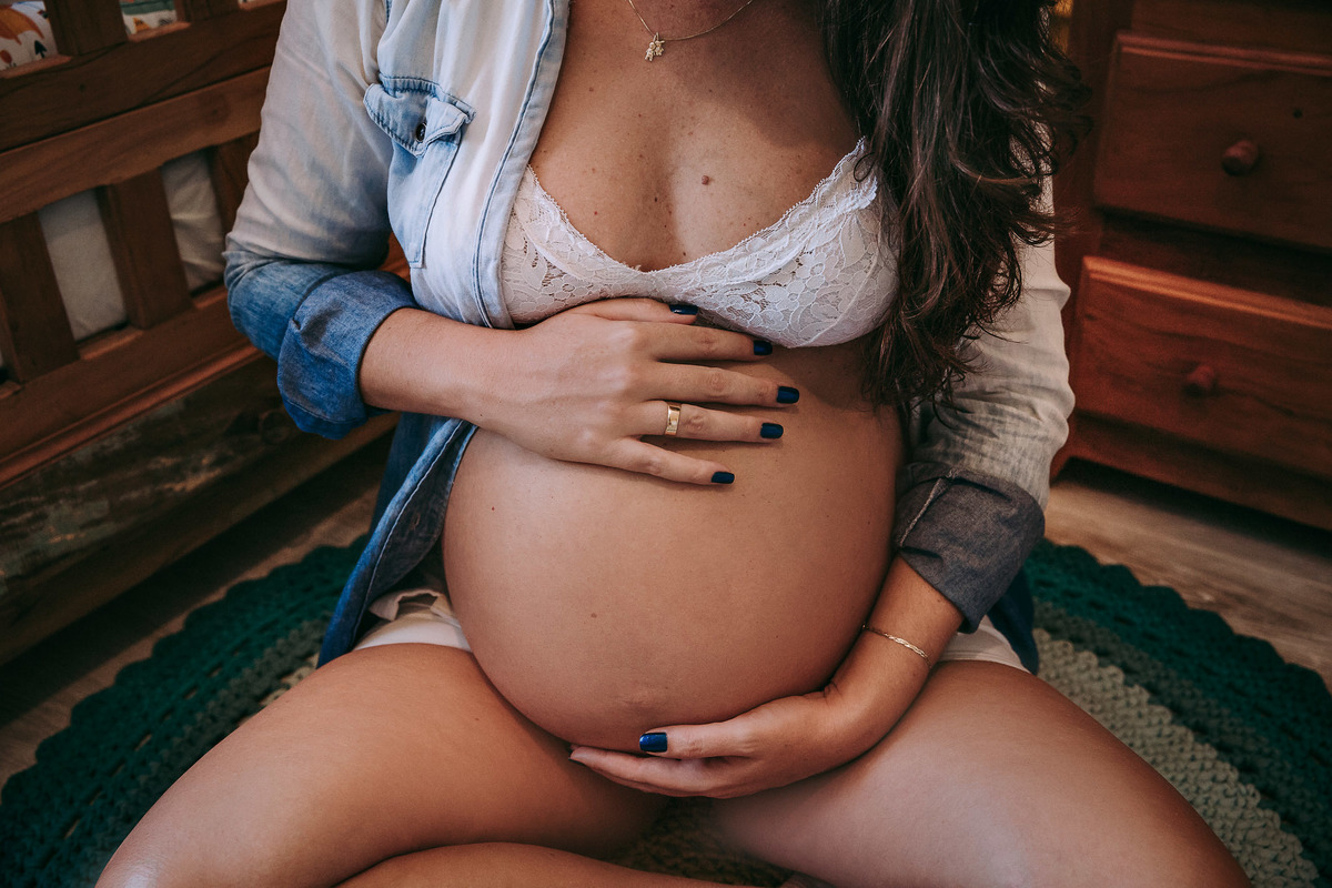 foto de close da barriga de gestante ela segura a barriga com as maos, uma na parte superios outra na inferior