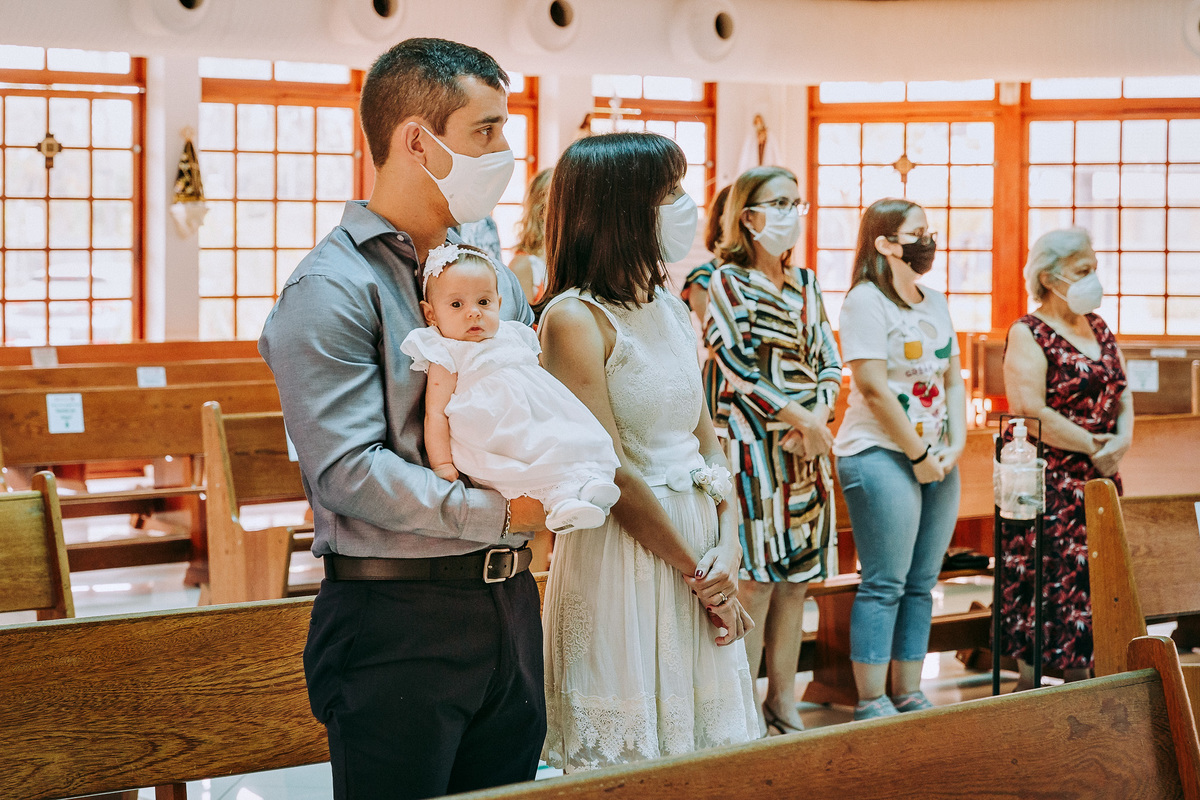 menina olha fixamente para camera fotografica durante a cerimonia de batismo na Paróquia São Marcelino de Champagnat enquanto todos acompanham a cerimonia