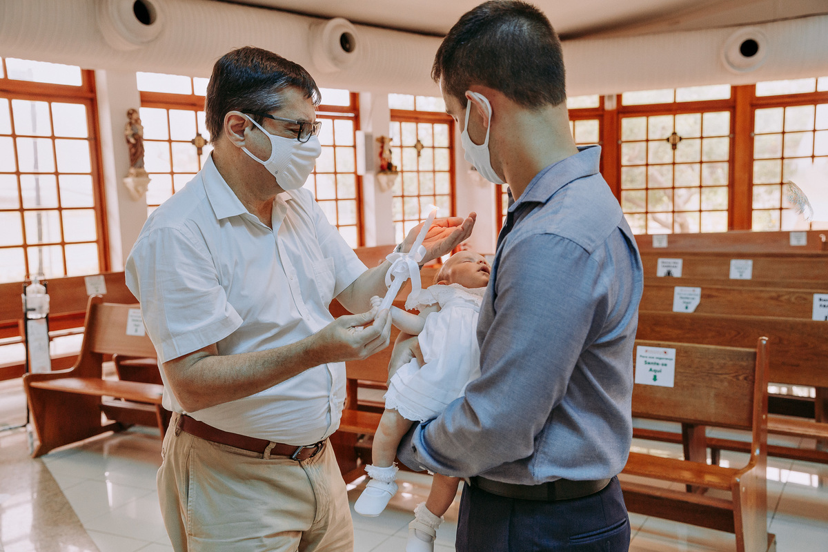 padrinho com a vela acesa rezando para sua afilhada enquanto ela é segura pelo pai na Paróquia São Marcelino de Champagnat