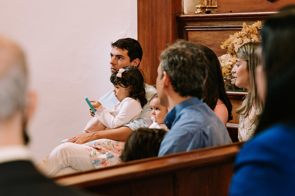 menina de tres anos brinca com celular sentada no colo de seu pai durante batista na paroquia nossa senhora da luz
