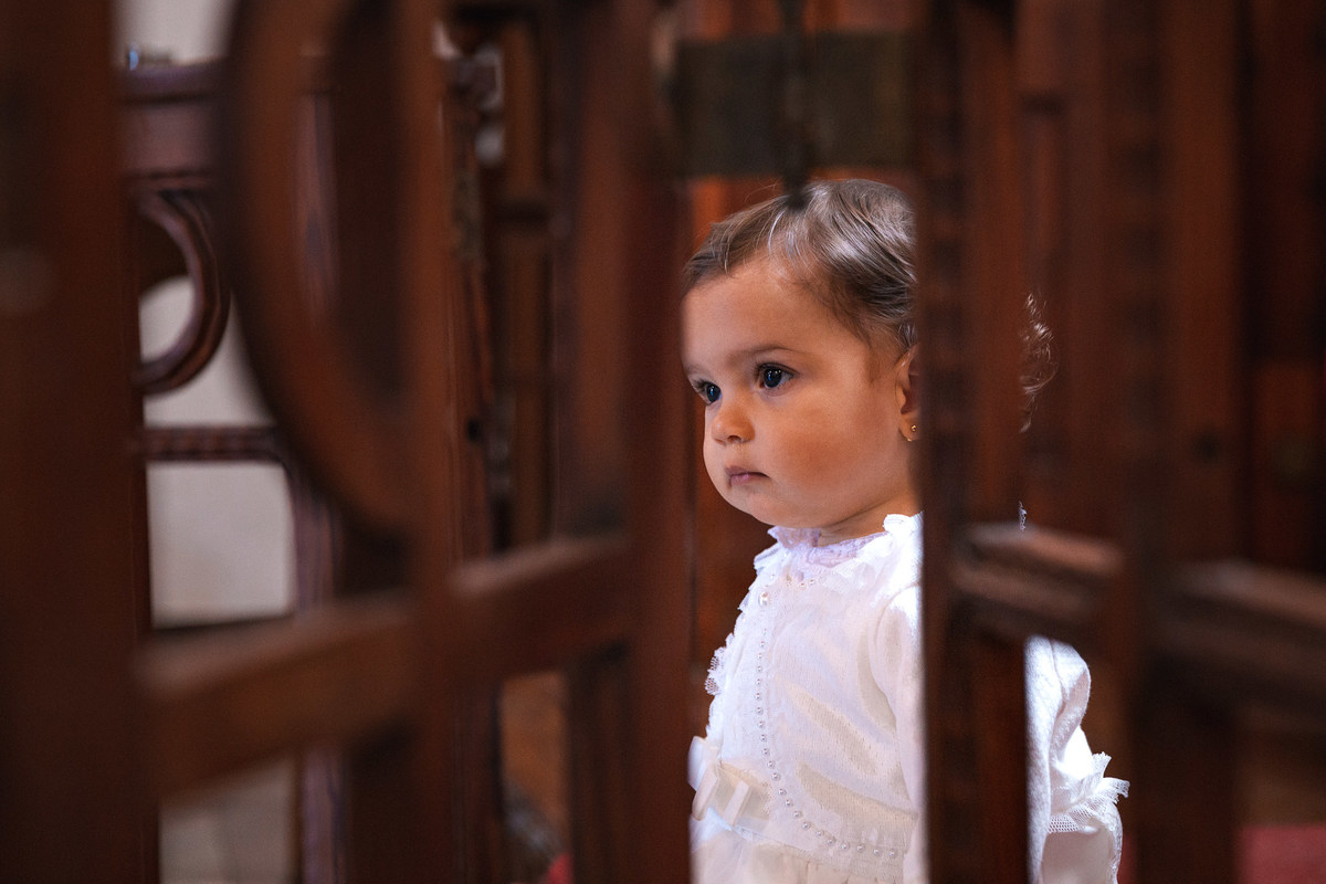 menina vestida de branco sendo fotografada por traz de grade de madeira