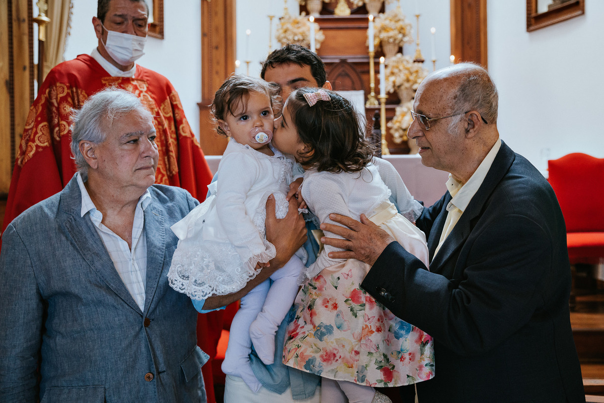 no altar, avós, pai e irmã beija criança sendo batizada