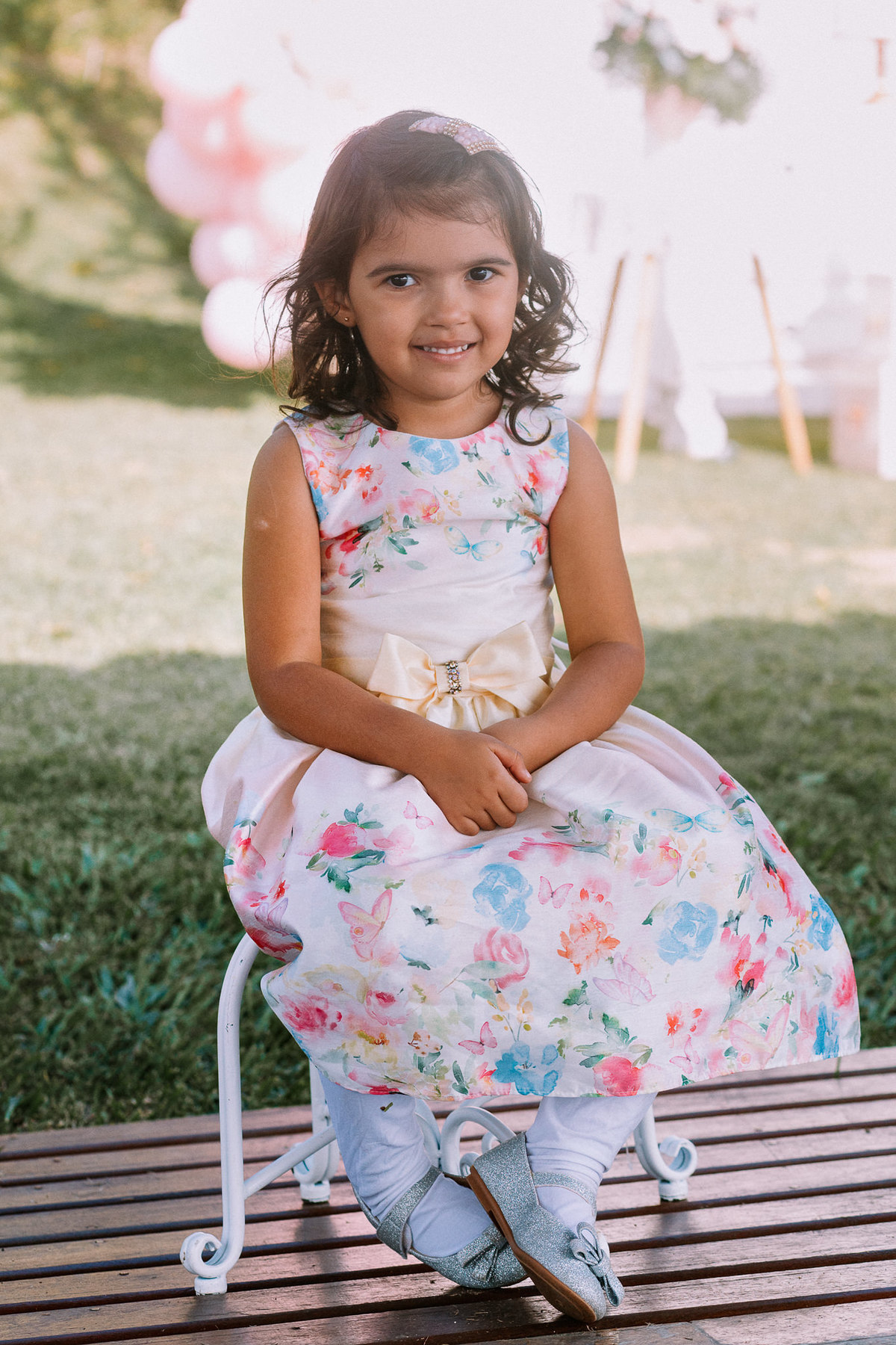 menina de vestido florido sentada em mini cadeira sorri para foto
