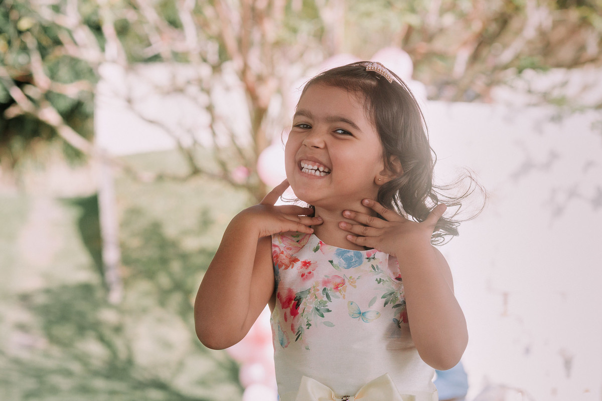 criança com as maos no pescoço sorri alegrmente para a camera, foto de meio corpo