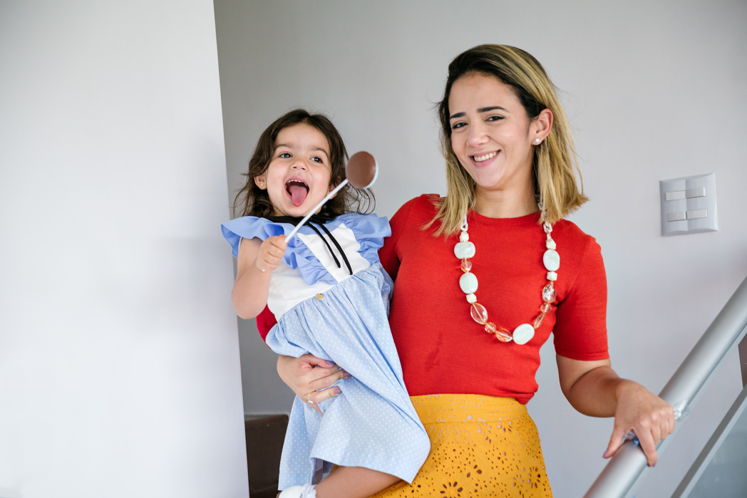 mae com a filha de tres anos no colo descendo as escadas de casa com um pirulito de chocolate na mão