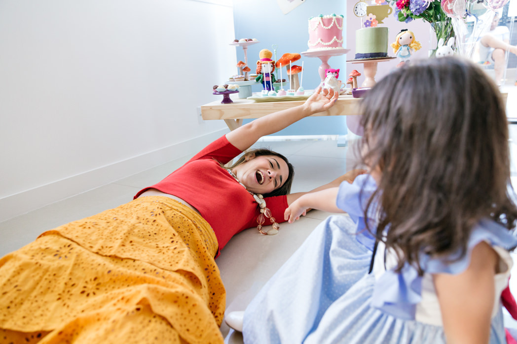 mae deitada no chão da sala brincando com sua filha durante sua festa de aniversario em casa