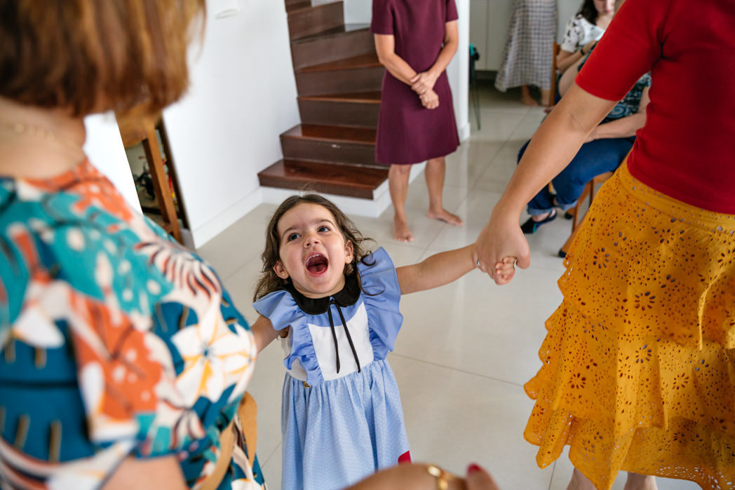 menina de 3 anos brincando de atirei o pau no gato e segurando a mão de duas tias
