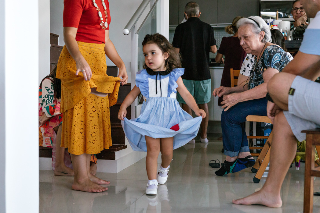 criança de 3 anos vestida de alice segura vestido enquanto passeia pela sala de sua casa