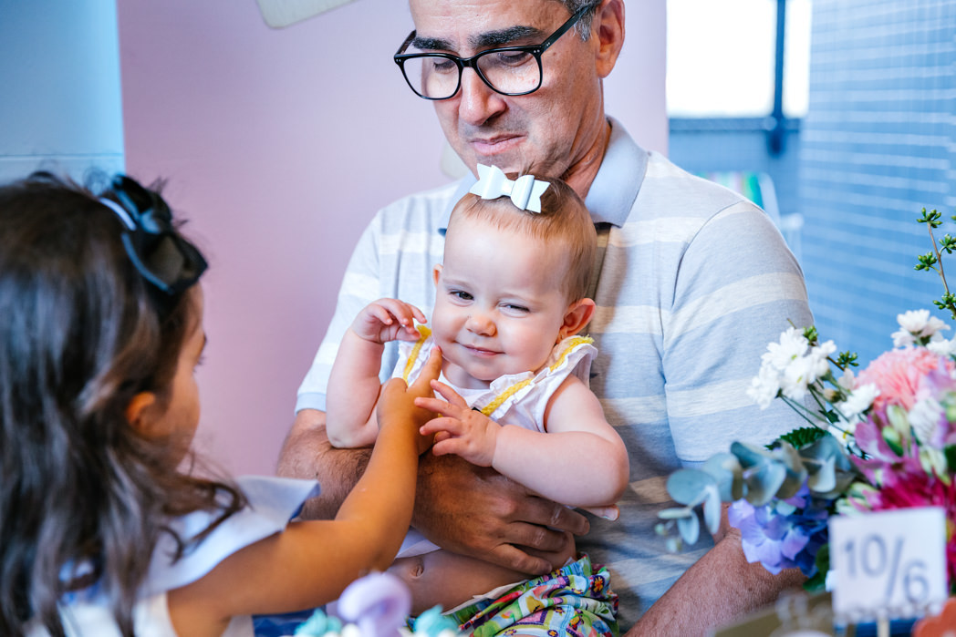 crinaça de 3 anos brinca com outra criança de 10 meses no colo do avo, bebe sorri