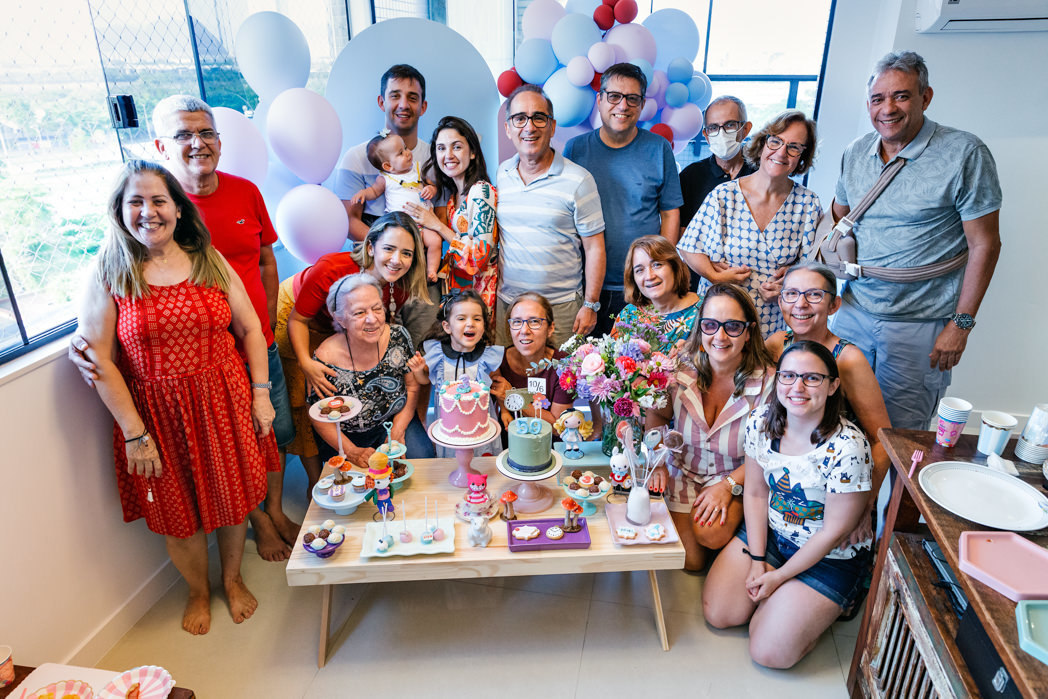 toda familia presente na festa de aniversario de 3 anos de maria alice posam para foto atras da mesa do bolo com tema alice no pais das maravilhas em condominio na barra da tijuca rj