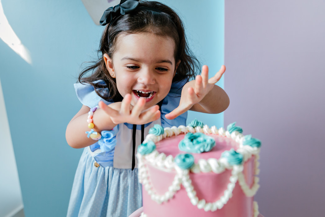 menina de tres anos vestida de alice ameaçando colocar as duas maos sobre o bolo e sorrindo