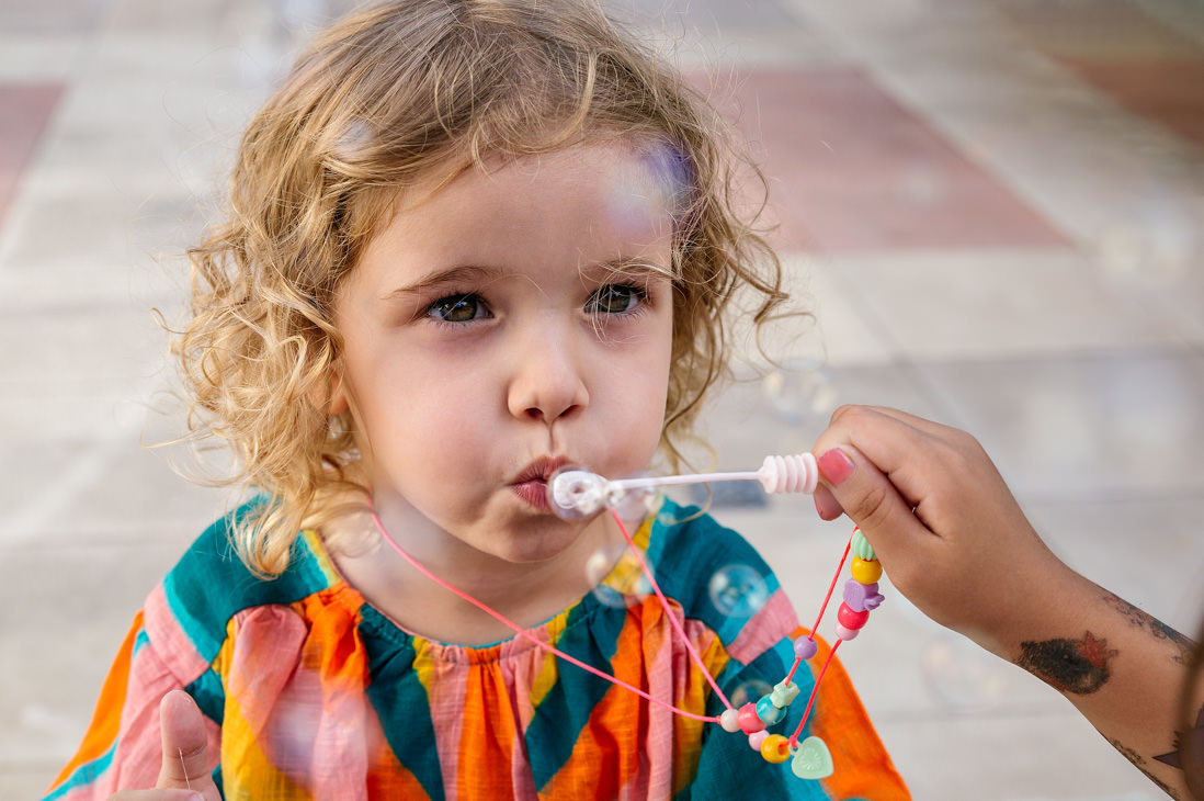 foto em plonge de menina de 3 anos loira assoprando bola de sabão