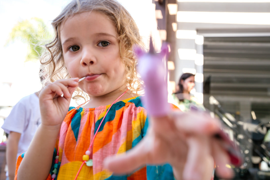 menina loira de 3 anos chupando pirulito aponta ponei de brinquedo para a camera fotografica