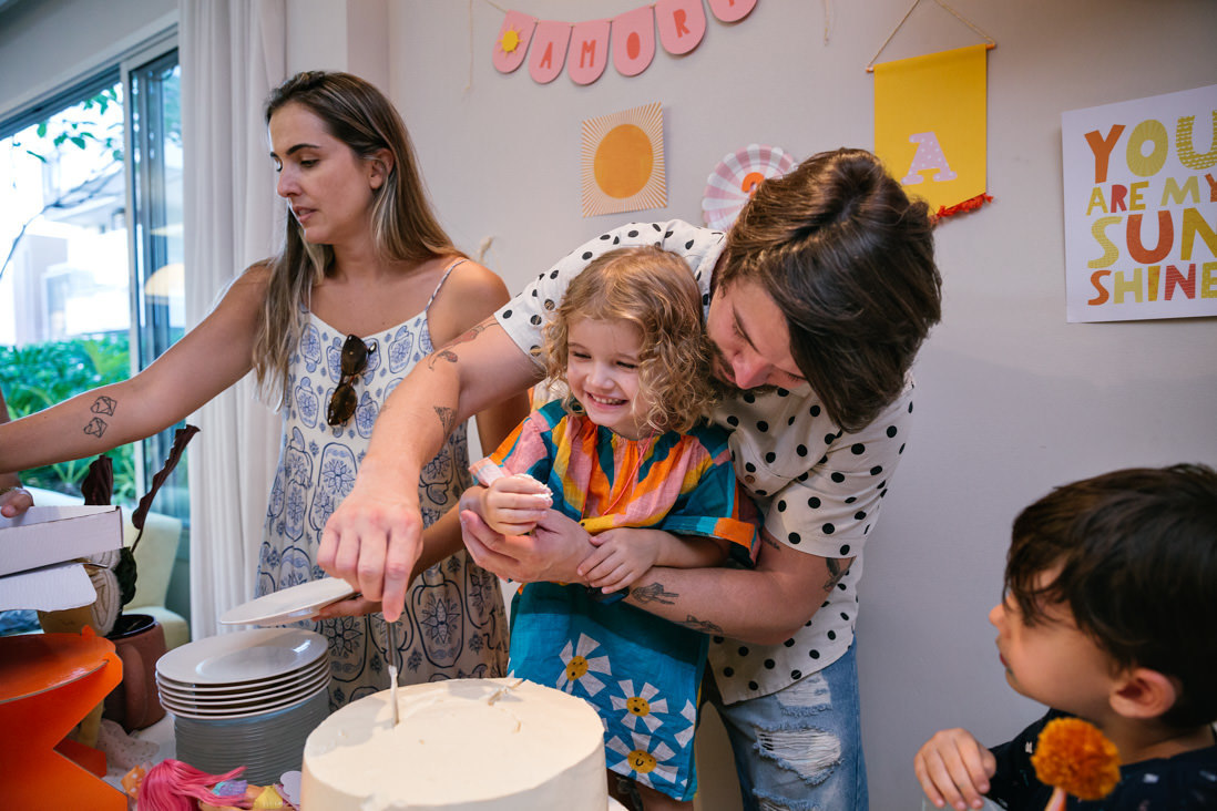 pai ajuda filha a cortar seu bolo na festa de seus tres anos