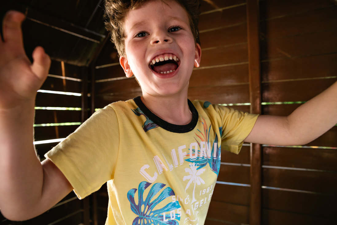 menino de camisa amarela e braços abertos sorri pra camera