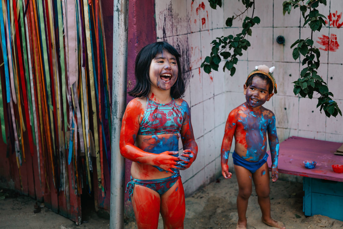 irmao olha admirado para irma sorrindo, ambos estao cobertos de tinta vermelha e azul