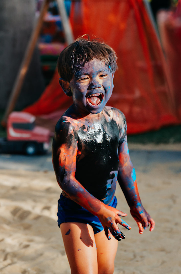 foto vertical menino de 3 anos coberto de tinta preta sorrindo