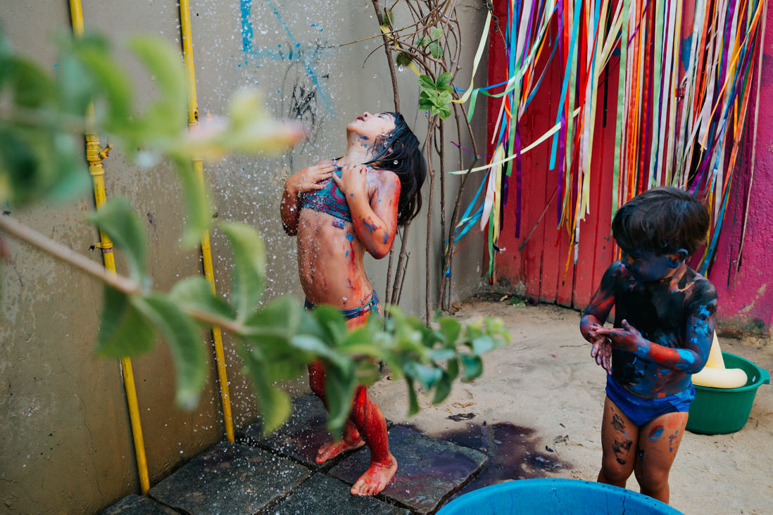 menina tira a tinta do corpo em chuveirao, ao seu lado menino coberto de tinda preta