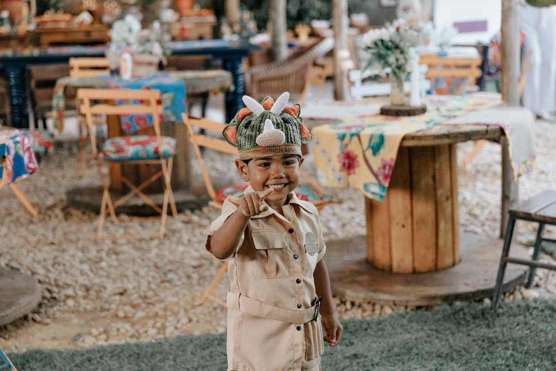 menino de 3 anos vestido de arqueologo aponta para mesa de seu bolo