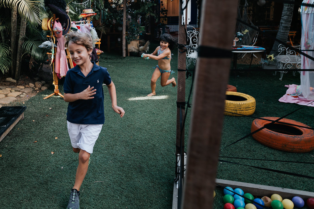 criança maior corre de menina com bola de gas cheia de agua