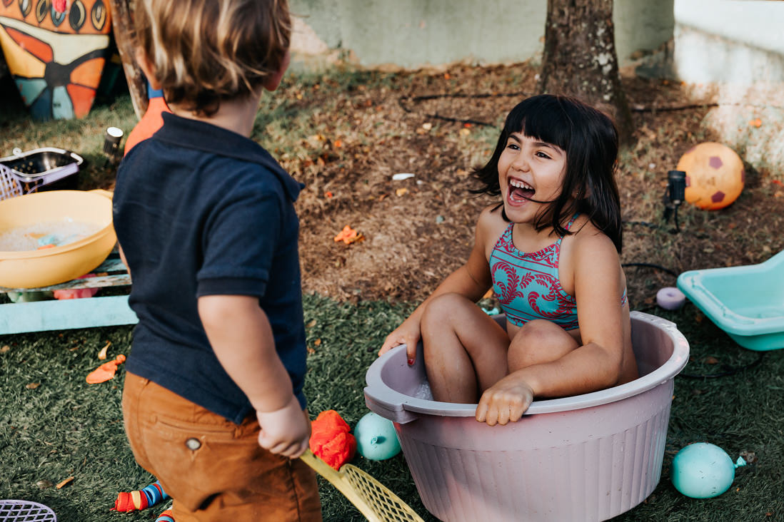 menina sentada em bacia com agua gargalha enquanto toma banho