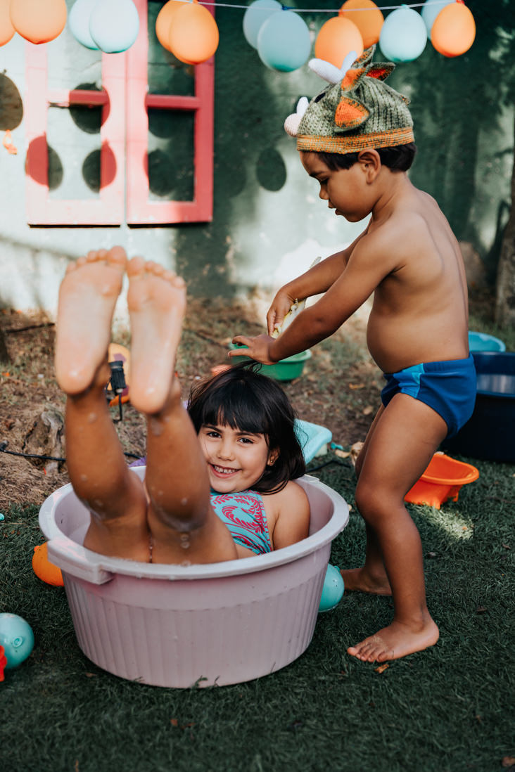 irmao menos brinca com cabelo da irma menor que esta sentada dentro de bacia com agua