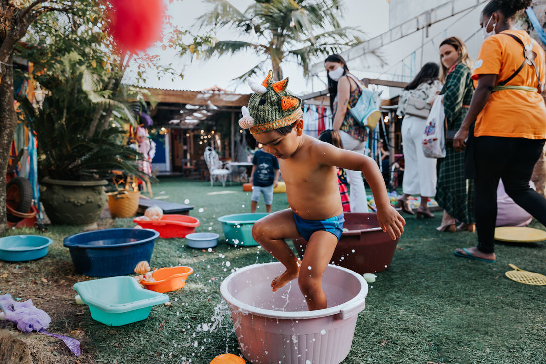 menino de 3 anos faz bagunça com agua em baciaenquanto é observado por adultos