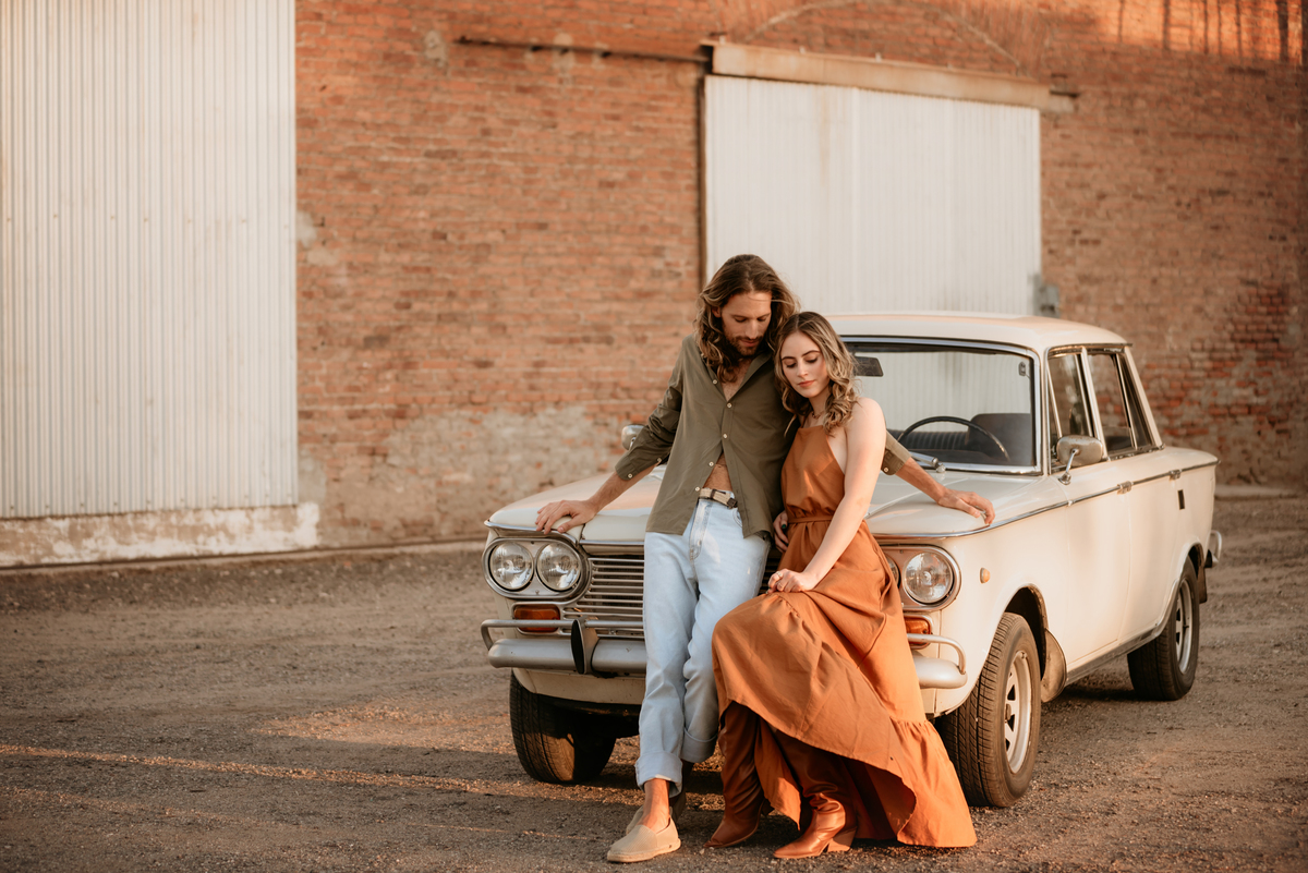 Atardecer con pareja apoyada en auto de colección. Pareja modelo. Amor.