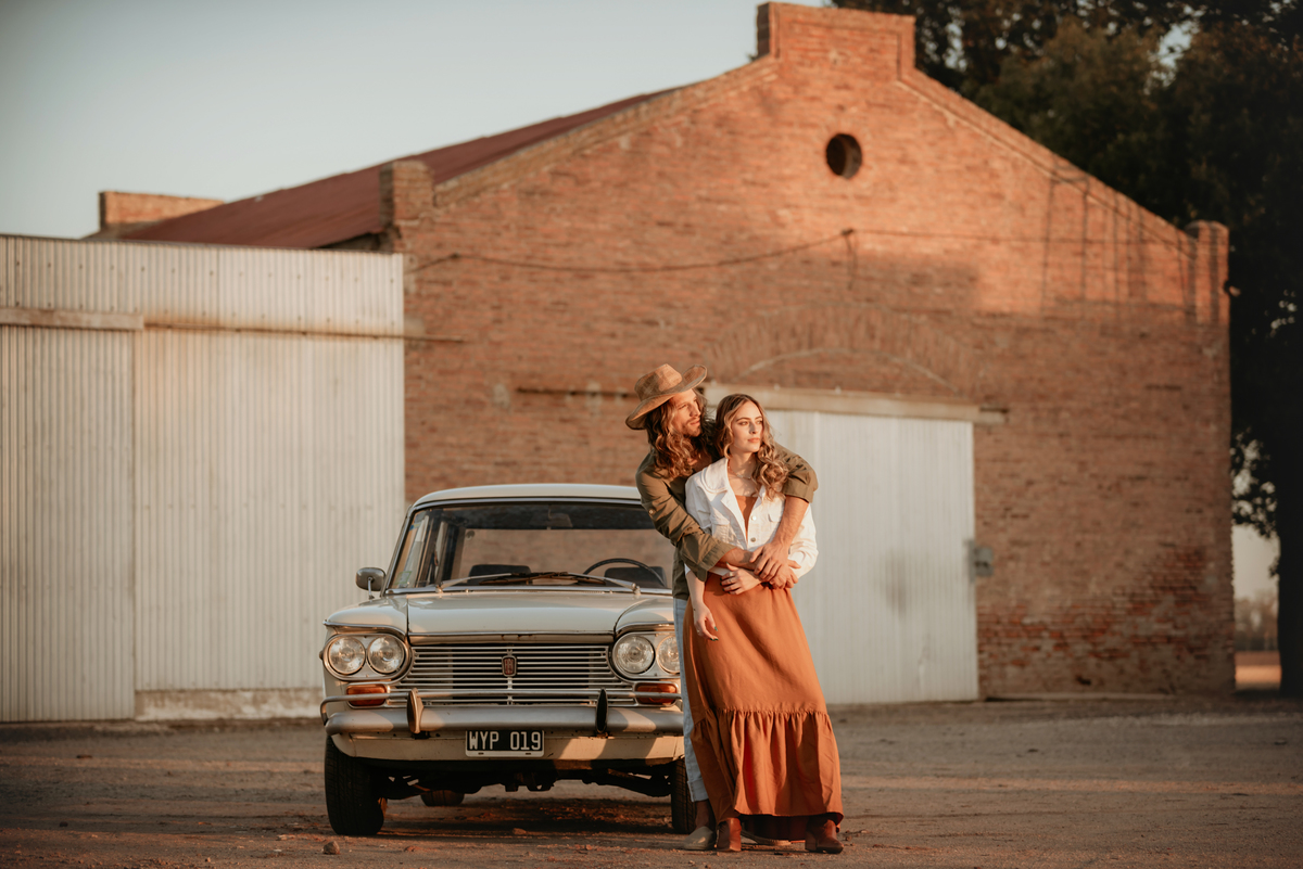 Atardecer con pareja apoyada en auto de colección. Pareja modelo. Amor. Él abrazando a ella.