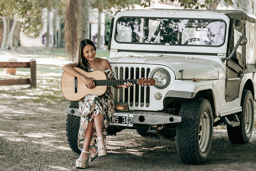 Quinceañera disfrutando de su book de fotos en una estancia, un día de verano con su hermoso vestido estampado y su guitarra. Sesión quince años. Barby Massei Fotografía.